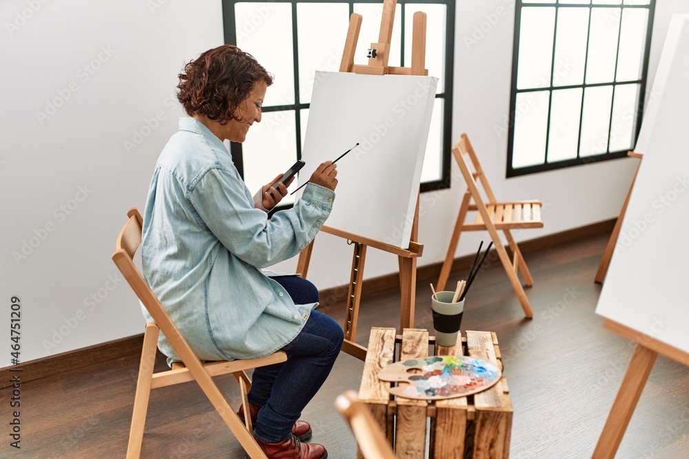Middle age hispanic artist woman using smartphone drawing at art studio. Middle age hispanic artist woman using smartphone drawing at art studio.