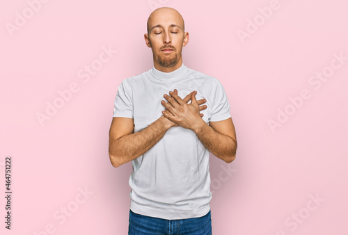 Bald man with beard wearing casual white t shirt smiling with hands on chest with closed eyes and grateful gesture on face. health concept.