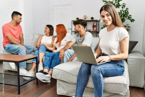 Group of young friends speaking sitting on the sofa. Woman smilimg happy and using laptop at home.