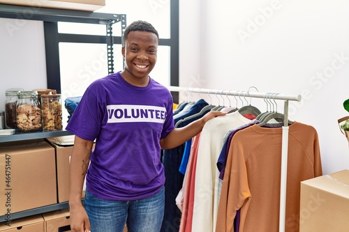 Young african man wearing volunteer t shirt at donations stand looking positive and happy standing and smiling with a confident smile showing teeth