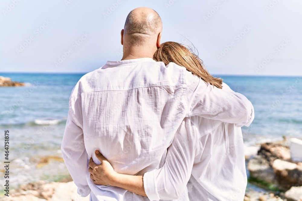 Middle age hispanic couple of husband and wife together walking by the beach on a sunny day. Hugging in love on vacation to the seaside. Middle age hispanic couple of husband and wife together walking by the beach on a sunny day. Hugging in love on vacation to the seaside.
