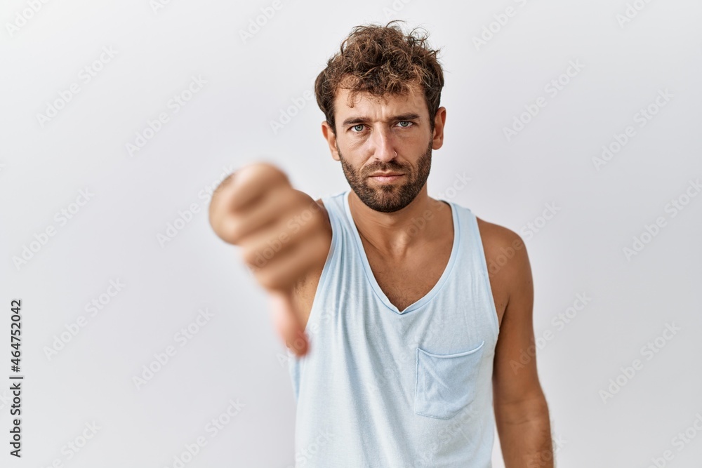 Young handsome man standing over isolated background looking unhappy and angry showing rejection and negative with thumbs down gesture. bad expression. Young handsome man standing over isolated background looking unhappy and angry showing rejection and negative with thumbs down gesture. bad expression.