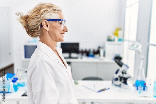 Middle age blonde woman working at scientist laboratory looking to side  relax profile pose with natural face with confident smile.
