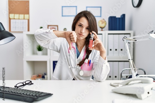 Young doctor woman holding electronic cigarette at medical clinic with angry face  negative sign showing dislike with thumbs down  rejection concept