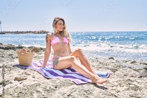 Young blonde girl wearing bikini sitting on the towel at the beach.