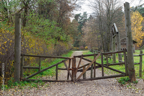 Wooden old rickety gates in the autumn park. Closed dirt road in the forest.