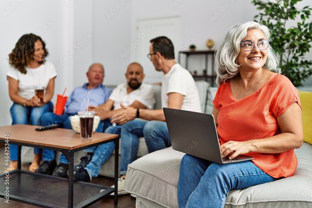 Fototapeta premium Group of middle age friends sitting on the sofa speaking. Woman smiling happy using laptop at home.