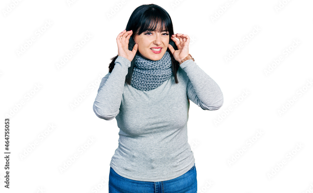 Young hispanic plus size woman wearing winter scarf trying to hear both hands on ear gesture, curious for gossip. hearing problem, deaf Young hispanic plus size woman wearing winter scarf trying to hear both hands on ear gesture, curious for gossip. hearing problem, deaf