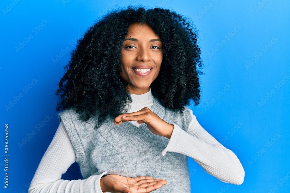 African american woman with afro hair wearing casual winter sweater gesturing with hands showing big and large size sign, measure symbol. smiling looking at the camera. measuring concept. African american woman with afro hair wearing casual winter sweater gesturing with hands showing big and large size sign, measure symbol. smiling looking at the camera. measuring concept.