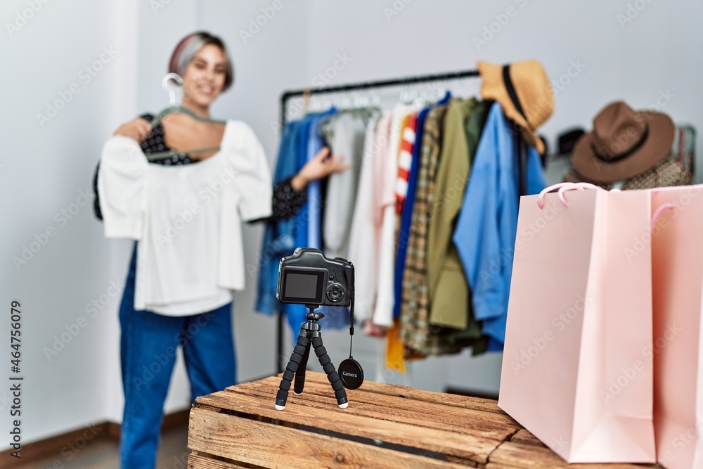 Young caucasian shopkeeper woman having video call showing clothes at clothing store. Young caucasian shopkeeper woman having video call showing clothes at clothing store.