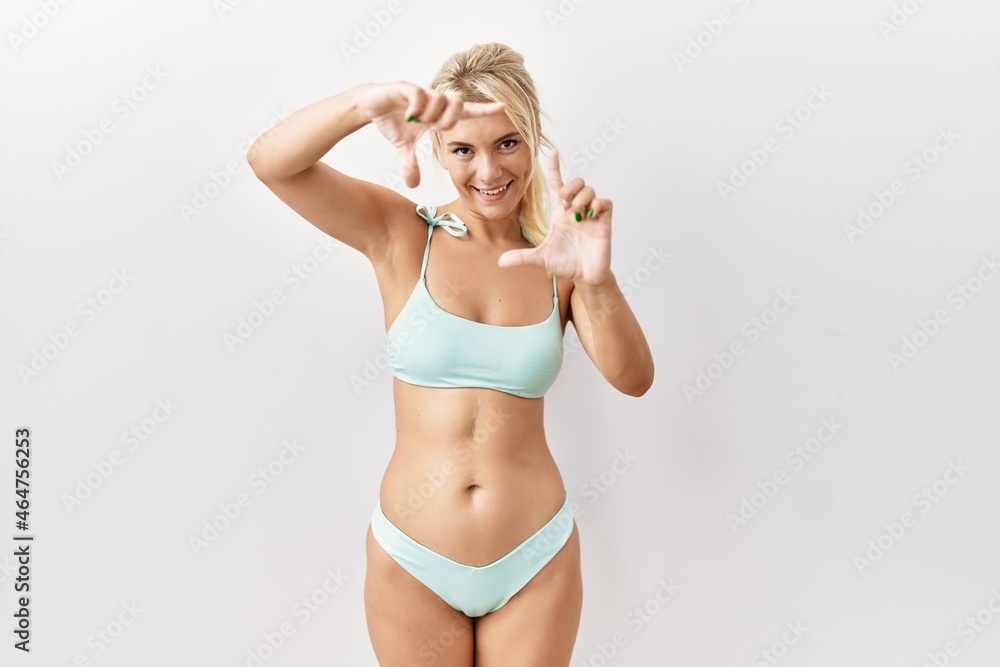 Young caucasian woman wearing bikini over isolated background smiling making frame with hands and fingers with happy face. creativity and photography concept. Young caucasian woman wearing bikini over isolated background smiling making frame with hands and fingers with happy face. creativity and photography concept.