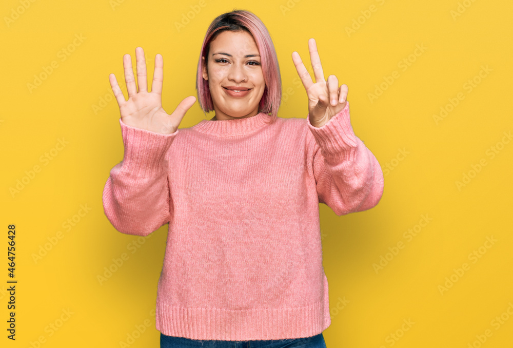 Hispanic woman with pink hair wearing casual winter sweater showing and pointing up with fingers number seven while smiling confident and happy. Hispanic woman with pink hair wearing casual winter sweater showing and pointing up with fingers number seven while smiling confident and happy.