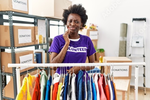 African young woman wearing volunteer t shirt at donations stand touching mouth with hand with painful expression because of toothache or dental illness on teeth. dentist