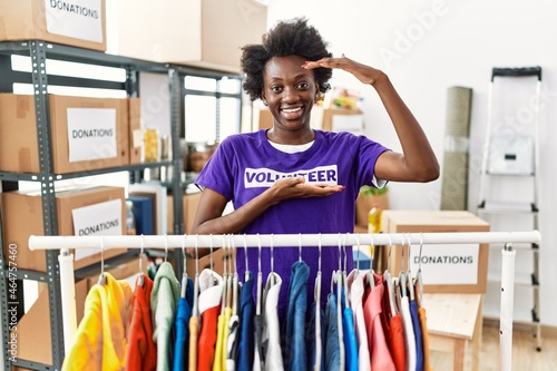 African young woman wearing volunteer t shirt at donations stand gesturing with hands showing big and large size sign, measure symbol. smiling looking at the camera. measuring concept.
