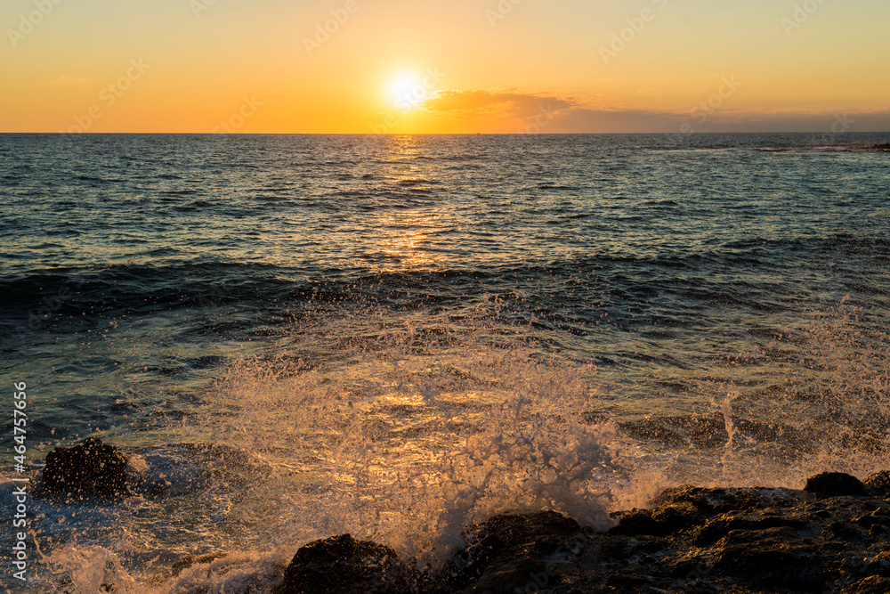 romantic sunset on the mediterranean coast with bursts of sea waves in the sun