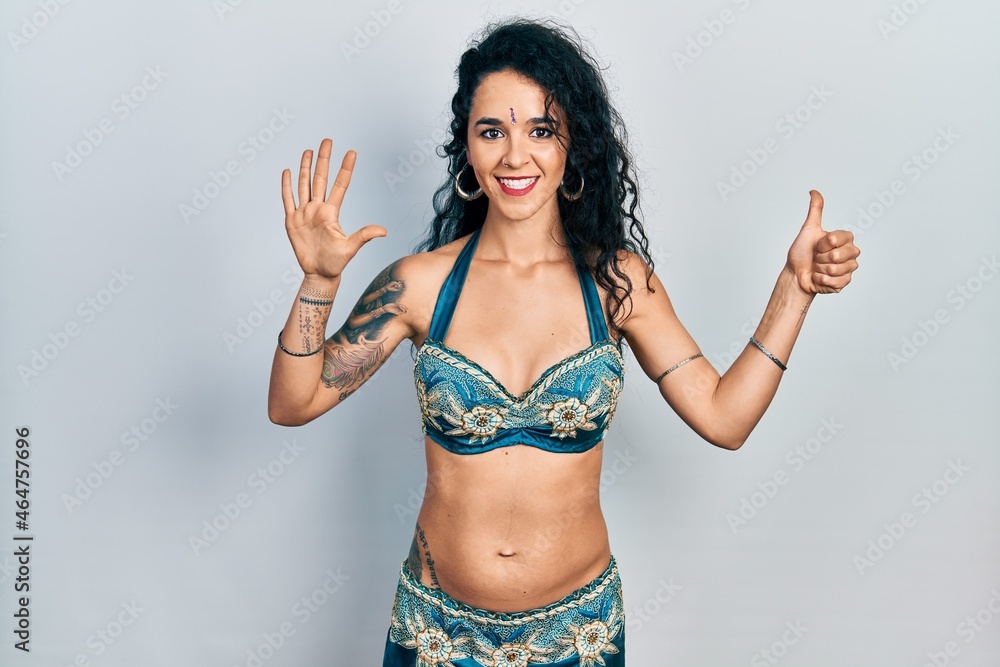 Fototapeta premium Young woman wearing bindi and traditional belly dance clothes showing and pointing up with fingers number six while smiling confident and happy.