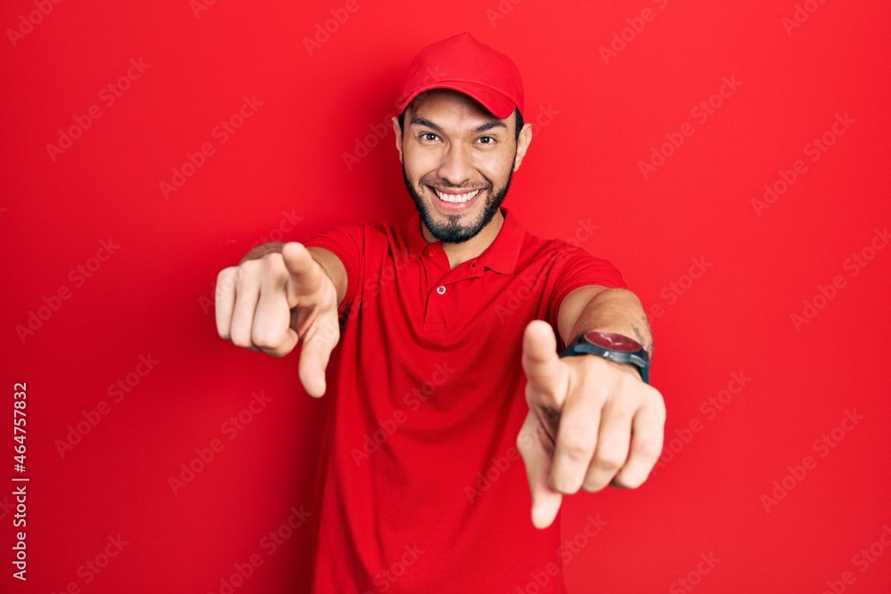 Hispanic man with beard wearing delivery uniform and cap pointing to you and the camera with fingers, smiling positive and cheerful Hispanic man with beard wearing delivery uniform and cap pointing to you and the camera with fingers, smiling positive and cheerful
