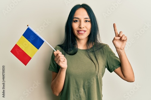 Young hispanic girl holding romania flag smiling with an idea or question pointing finger with happy face, number one