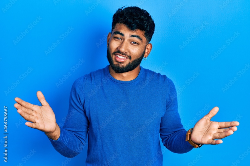Arab man with beard wearing casual blue sweater clueless and confused expression with arms and hands raised. doubt concept. Arab man with beard wearing casual blue sweater clueless and confused expression with arms and hands raised. doubt concept.