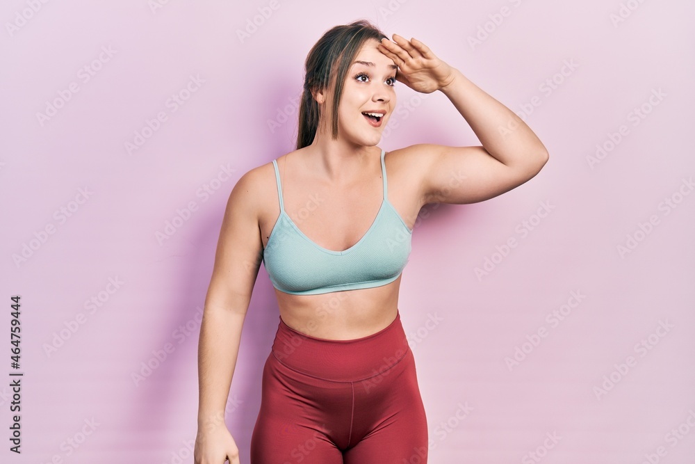 Young hispanic girl wearing sportswear very happy and smiling looking far away with hand over head. searching concept. Young hispanic girl wearing sportswear very happy and smiling looking far away with hand over head. searching concept.