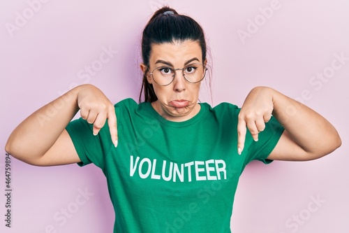 Young hispanic woman wearing volunteer t shirt pointing down looking sad and upset, indicating direction with fingers, unhappy and depressed.