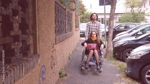 help, assistance - slow motion on young man accompaning his girlfriend using wheelchair for a walk in the city photo