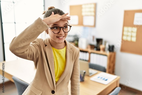 Young brunette teenager wearing business style at office very happy and smiling looking far away with hand over head. searching concept.