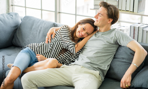 Young romantic couple embracing, sitting on cozy couch in living room relaxing at home, bonding relationship. Family portrait smiling overjoyed wife and happy closed eyes husband stay home together.