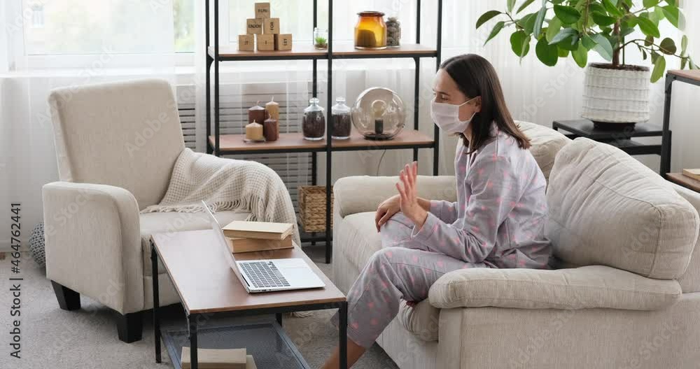 Cautious woman in protective medical face mask video chatting using laptop at home Cautious woman in protective medical face mask video chatting using laptop at home