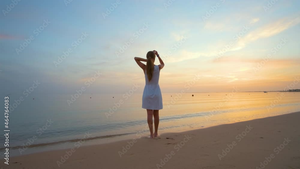 Lonely young woman standing on sandy beach by seaside enjoying warm tropical evening Lonely young woman standing on sandy beach by seaside enjoying warm tropical evening