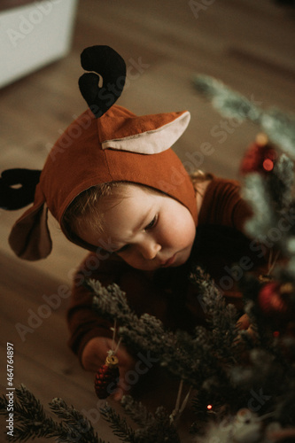 Toddler baby girl in rudolph reindeer costumes decorating Christmas tree