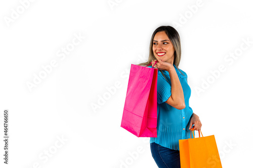 Beautiful young woman looking into empty space, with happy expression and colorful shopping bags in both hands. Copy space. White background.