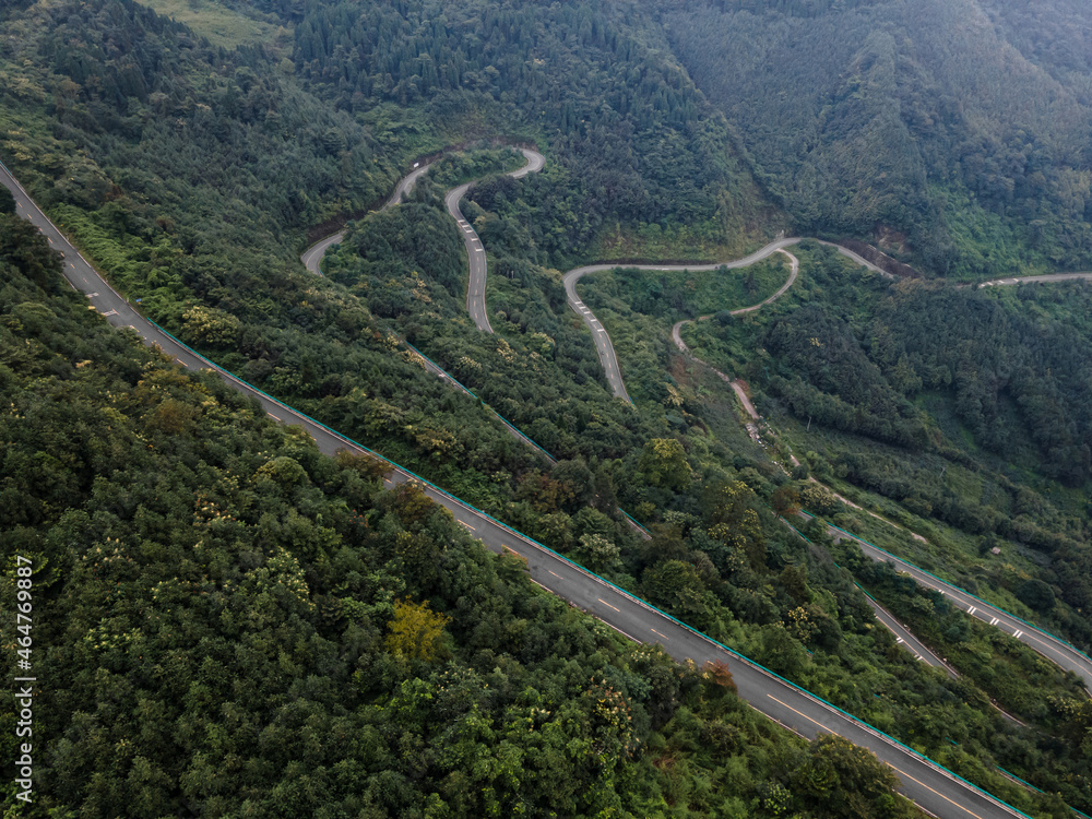 Curved serpentine asphalt automobile road on the way to Qingcheng mountain in Sichuan province, China. Misty day, drone aerial top down view. Surrounded by pine tree forests.