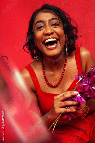 Malaysian Indian individual dressed in red clothing, against a red background, posing and laughing photo