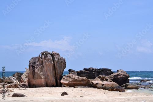 Large stones on a sandy beach against the background of the sea and sky on a sunny day