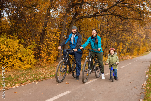 family with child riding on bikes together in autumn park
