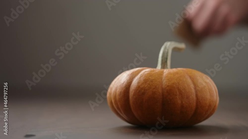 Slow motion man hand put thanksgving card next to small orange pumpkin on walnut table photo