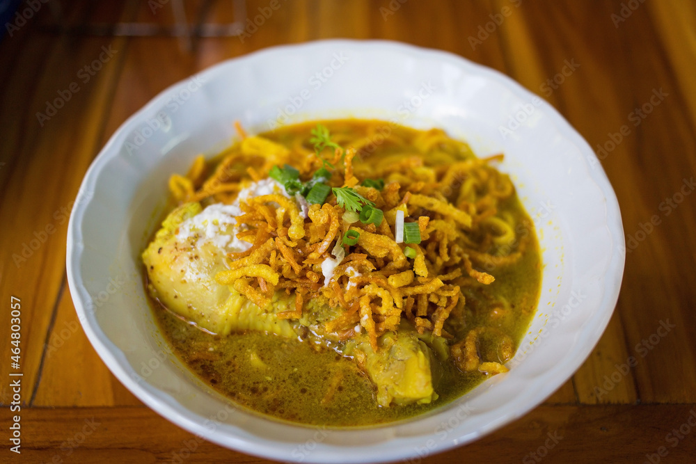 Curried noodle soup with chicken (Khao Soi Kai) is a Northern Thai food style in white cup on wooden background.