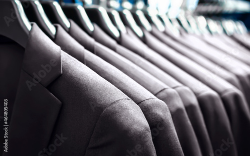 Suit jackets in hanger in men fashion and apparel store. Row of many clothes in rack or wardrobe. New stylish collection in elegant luxury retail shop. Expensive custom tailor made professional wear.