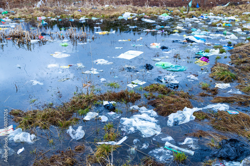 Fototapeta Naklejka Na Ścianę i Meble -  Verkhnie-Sergi, Russia - May 02, 2021. a lot of garbage and plastic bags in a puddle of water on the field. grass and packages. danger of pollution of the environment