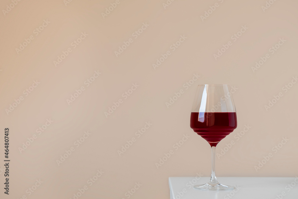 Glass of red wine on white table on beige neutral background with space for text, simple elegant composition Glass of red wine on white table on beige neutral background with space for text, simple elegant composition