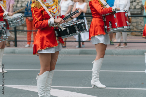 Street performance of festive march of drummers girls in red costumes on city street. Young girls drummer in red vintage uniform at the parade