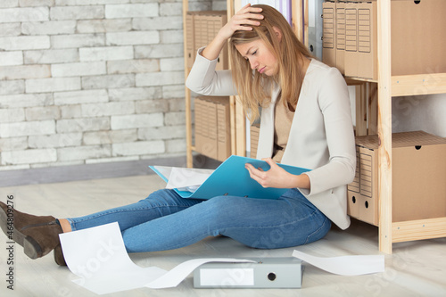 overwhelmed woman on floor surrounded by folders searching for paperwork