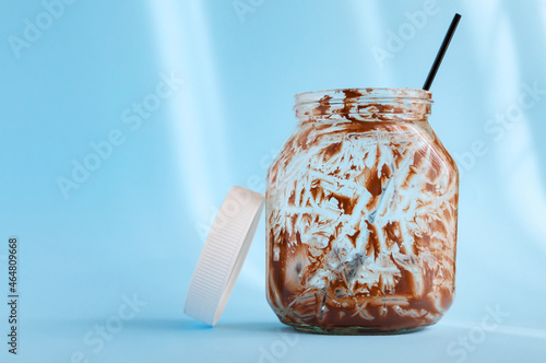 Empty jar of chocolate nut spread with a spoon on a light blue background. Favorite delicacy, traditionally for breakfast, popular sweet paste for sandwiches and baked goods.