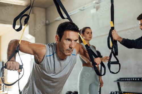 Fit man trains push ups with suspension trx straps at gym club.