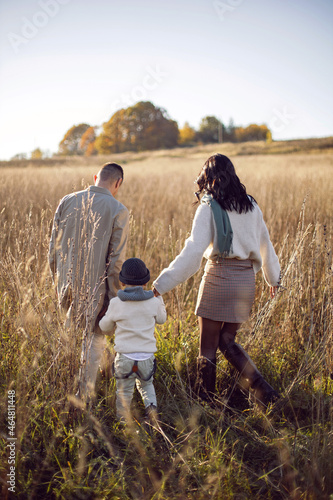 family of three with a boy child mom and dad are standing on a field in autumn at sunset