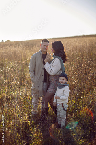 family of three with a boy child mom and dad are standing on a field in autumn at sunset