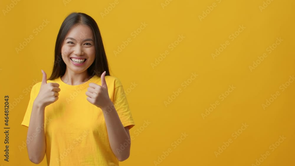 Excited Chinese Woman Pointing Fingers Aside Gesturing Thumbs-Up, Yellow Background Excited Chinese Woman Pointing Fingers Aside Gesturing Thumbs-Up, Yellow Background