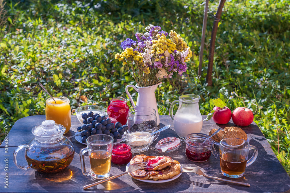Tea, pancakes, milk and jam on the breakfast table in the autumn garden, close up