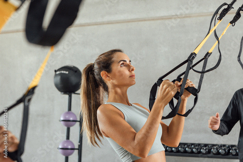 Beautiful woman concentrated with suspension strap workout at gym hiit class.